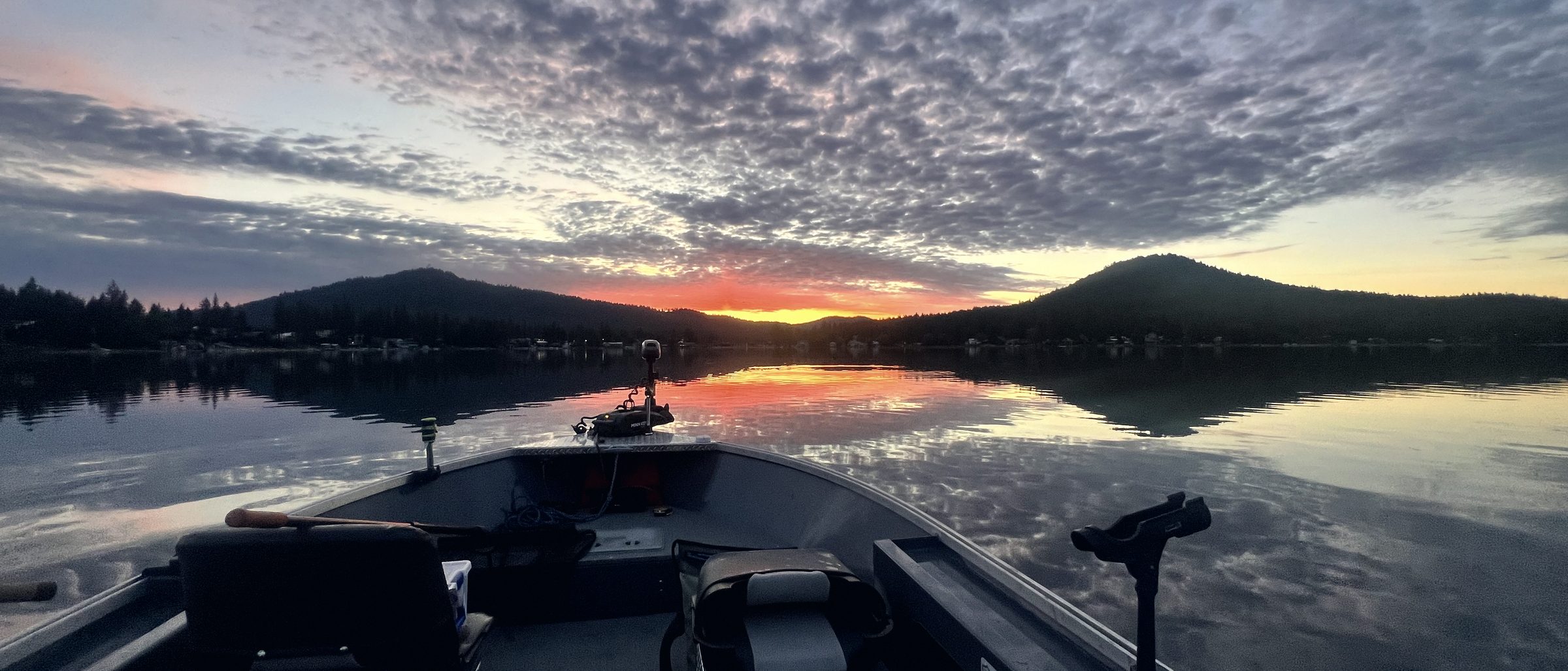 The bow of a boat at dawn with the console silhouetted against a low sun.