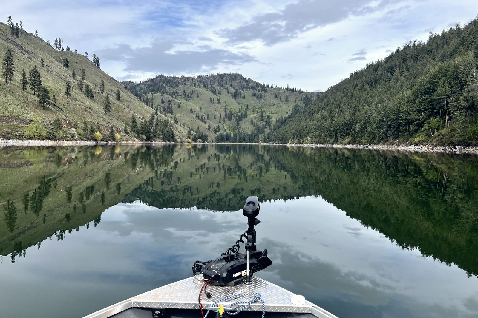 Mirror-flat water at dawn seen over the bow of a boat with the trolling motor deployed.