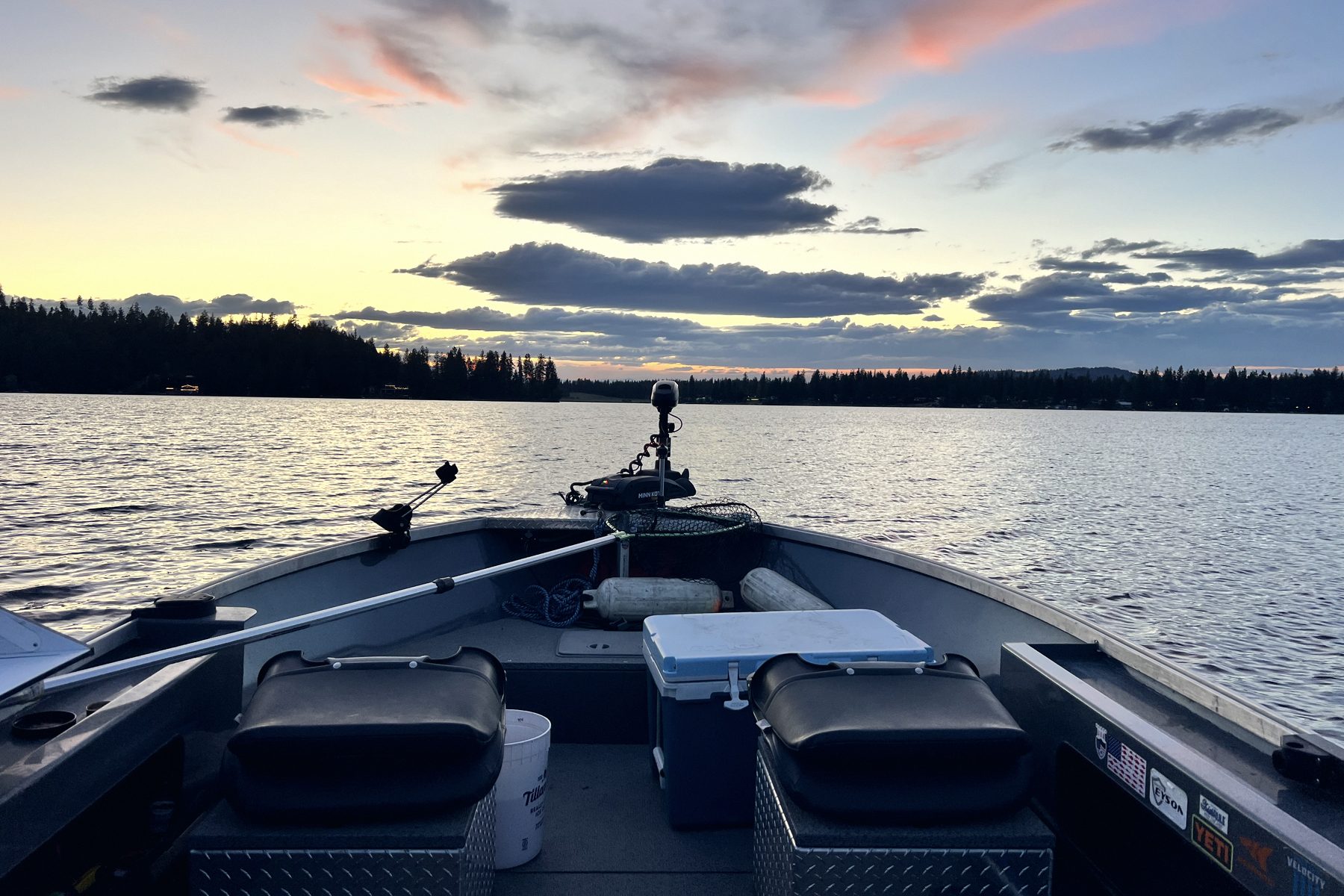 An empty boat cockpit at first light, rods stowed and the water flat ahead.