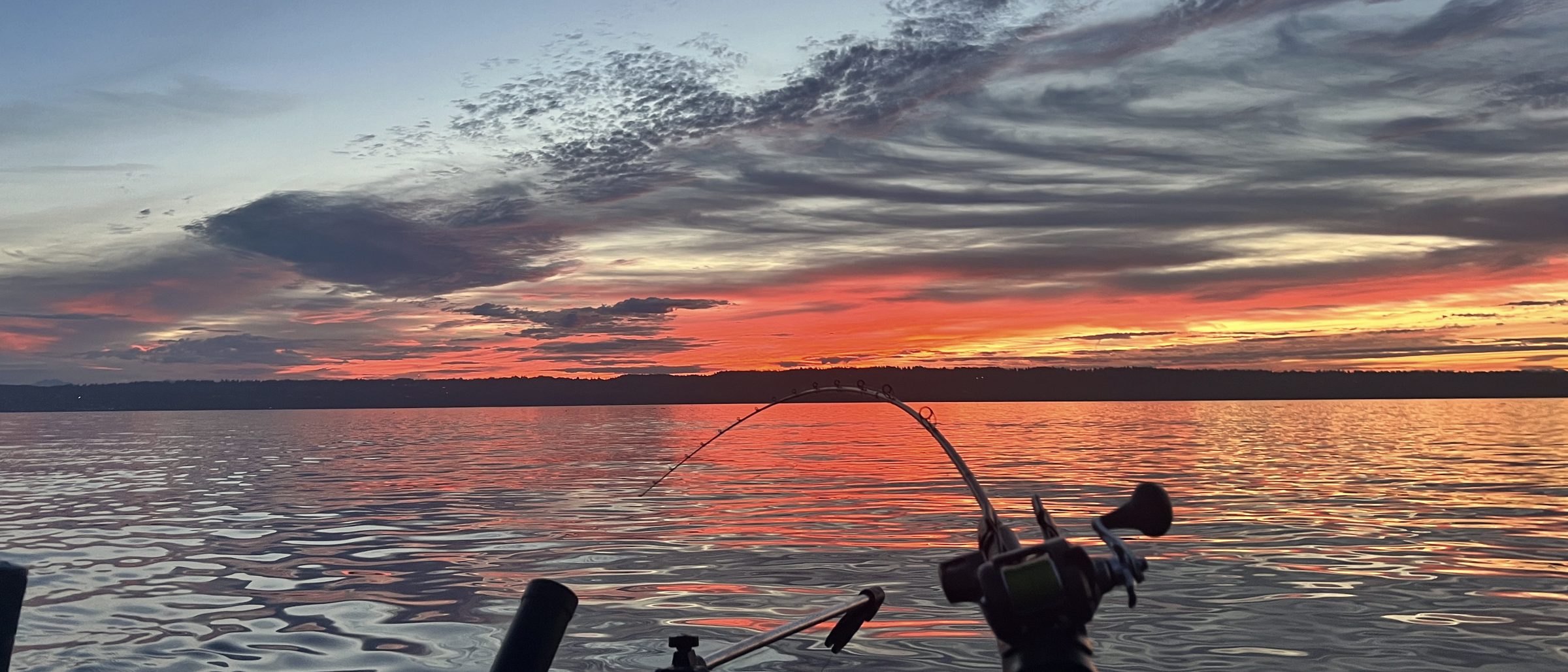 A rod bent over the gunwale at daybreak with the water lit behind it.