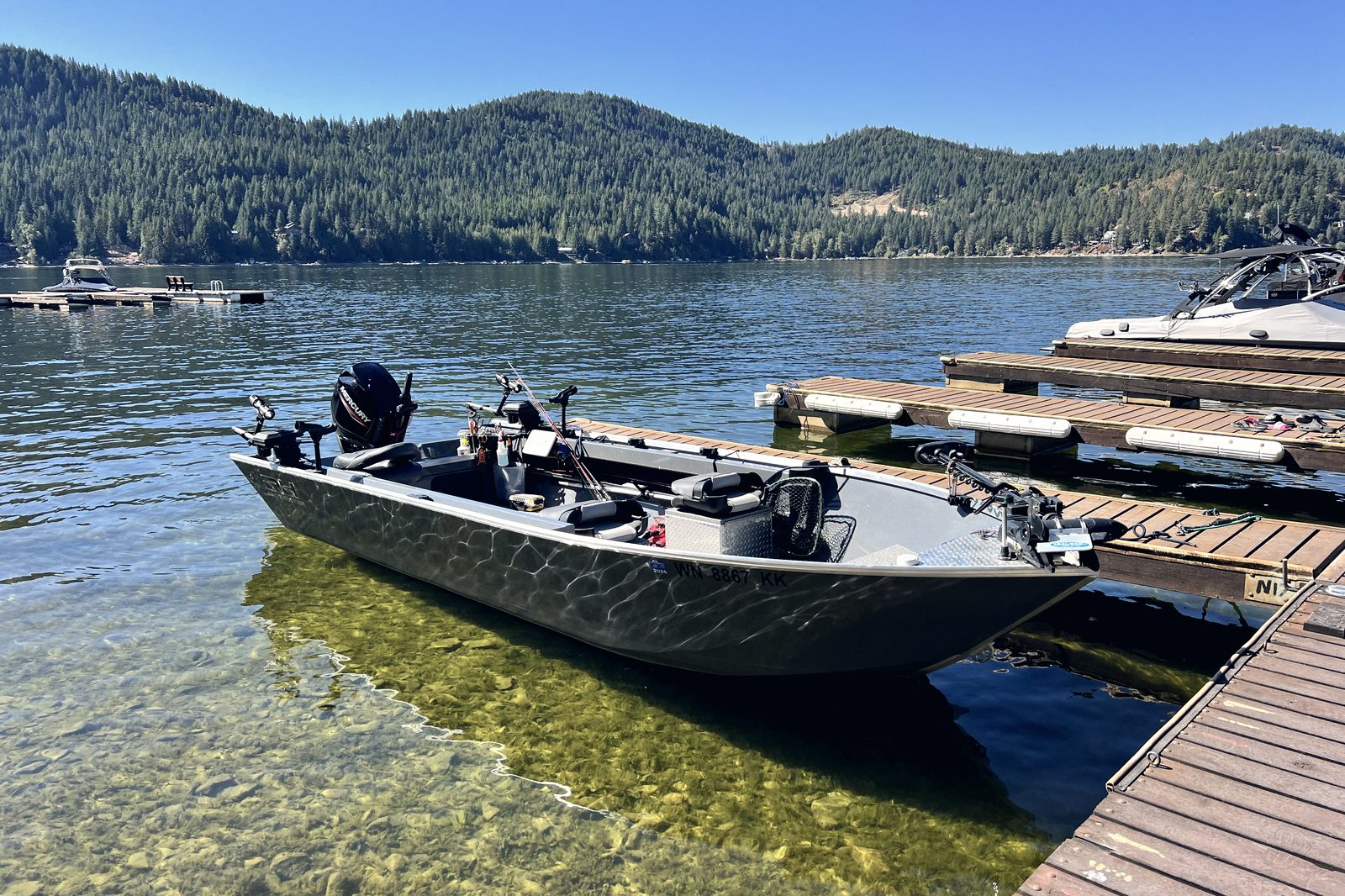 A fishing boat tied at a dock in clear green water on a bright day.