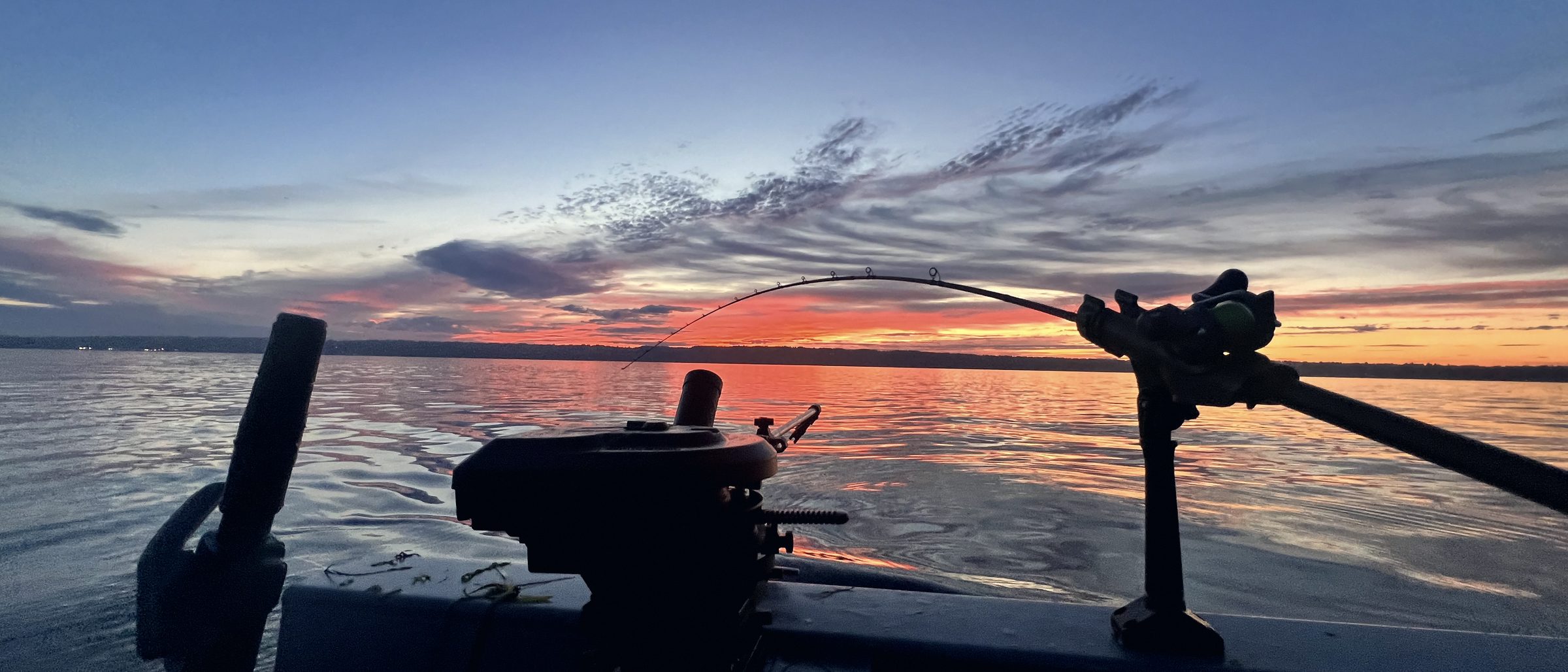 A rod and downrigger silhouetted over the gunwale against a low dawn sky.