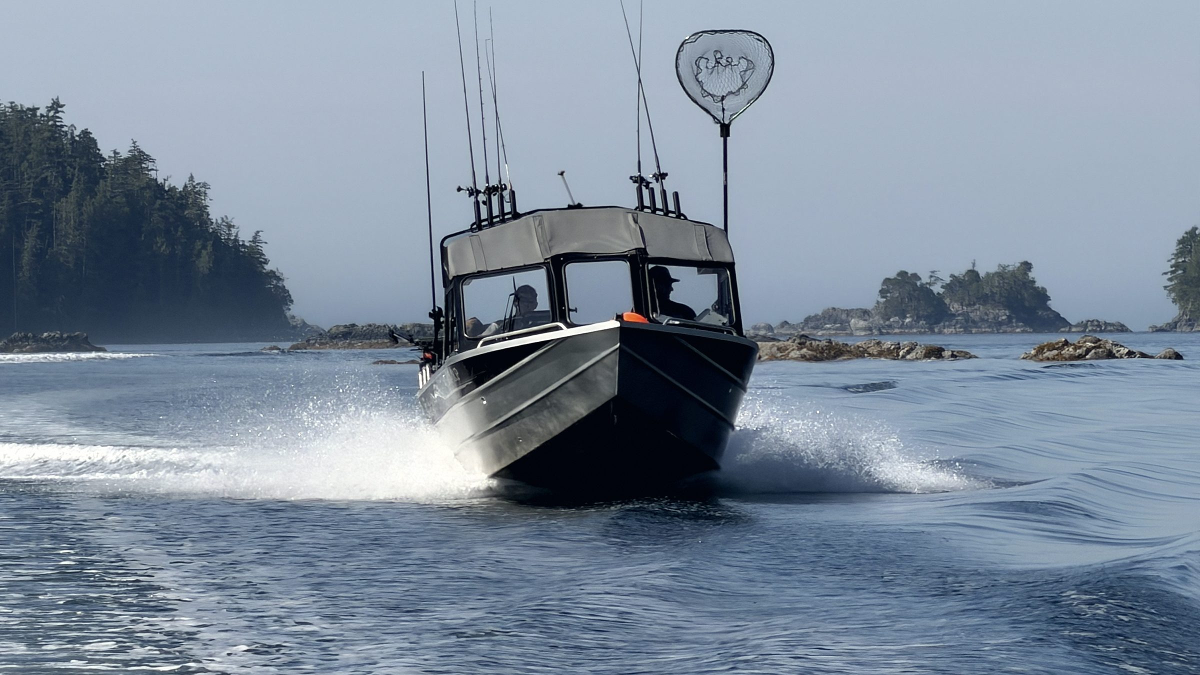 A fishing boat running hard through morning fog past a rock outcrop in Pacific Northwest water.