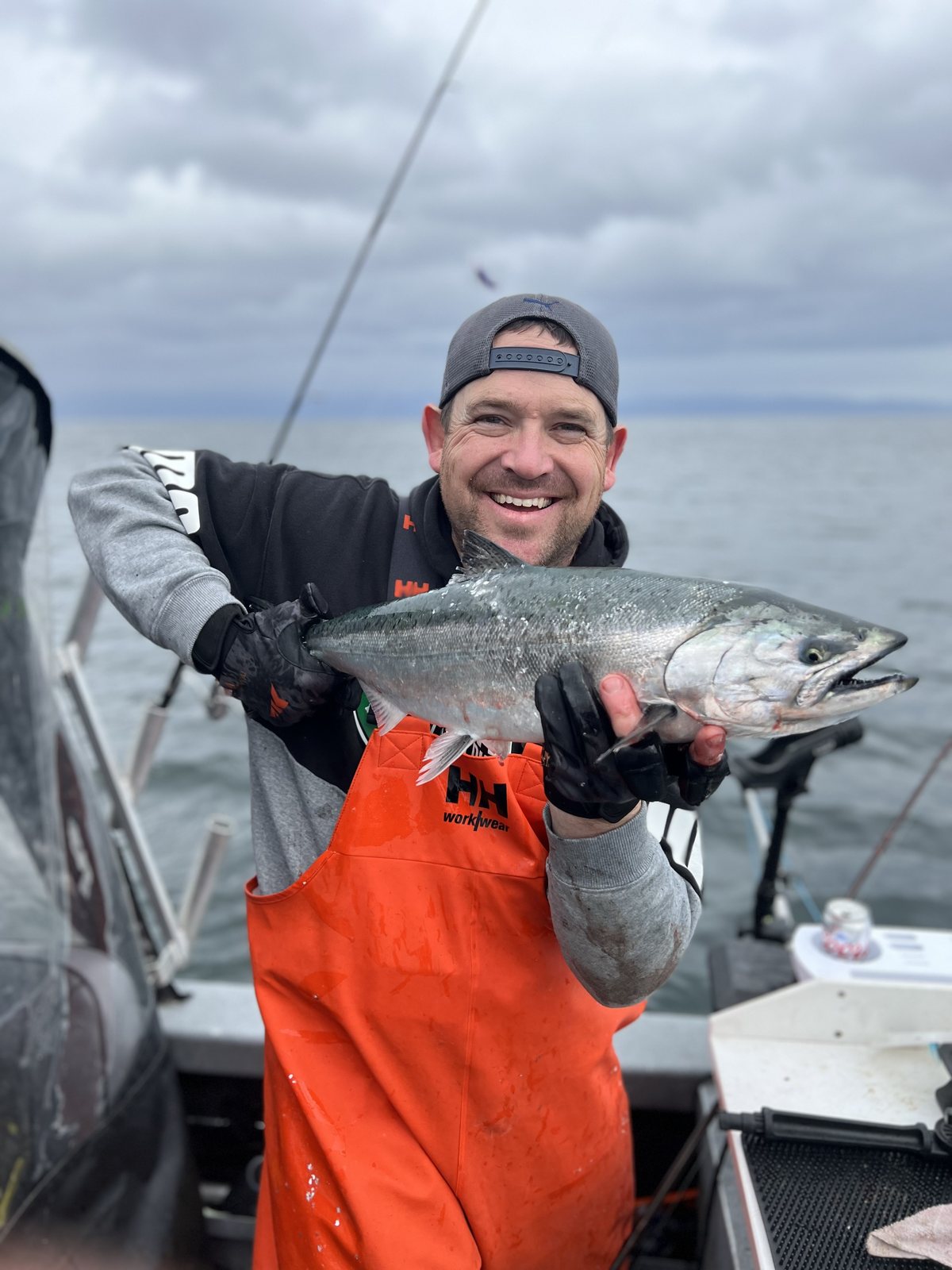 Jeremy Russell holding a bright chrome salmon in the boat, grinning, open water behind him.