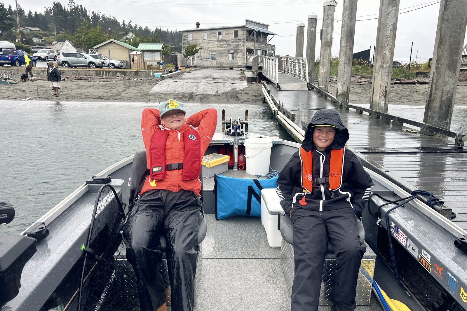 Two young anglers in float coats waiting out weather in the boat at the dock.